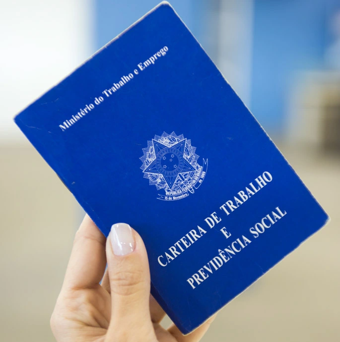 a mão de uma mulher segurando uma carteira de trabalho